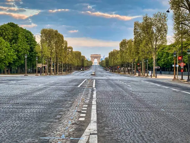 Paris, France - April 11, 2020 - View of the avenue des Champs-Elysées completely empty during the confinement linked to the health crisis of the coronas virus. In the foreground, the cobblestones of the avenue covering the road and the first stores located on the sides of the Champs-Elysées are visible. In the background, the Arc de Triomphe under a sunrise is visible.