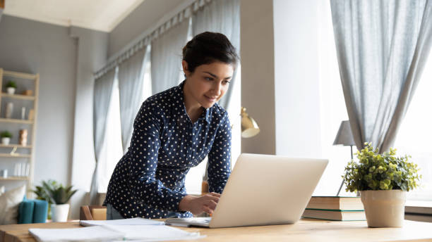 istock Smiling Indian girl standing at desk, working on laptop 1218223729