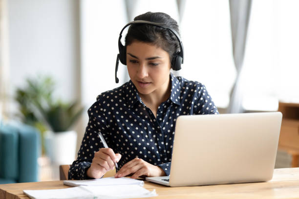 istock Focused Indian girl wearing headset writing notes, studying online 1218223749