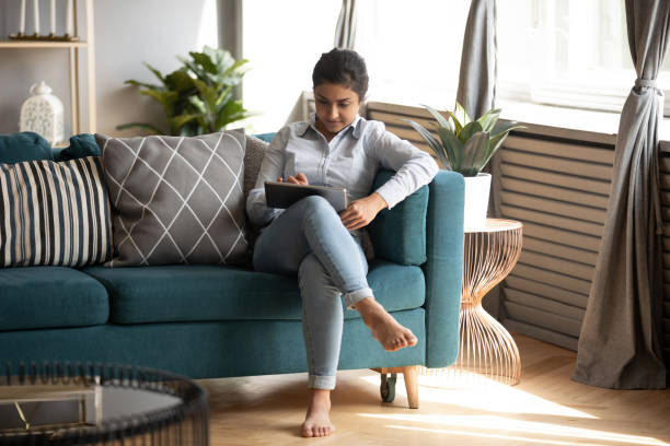 istock Indian young woman using computer tablet, sitting on cozy sofa 1218223834