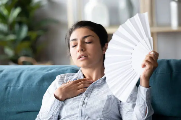 Photo of Overheated Indian woman waving paper fan, feeling unwell