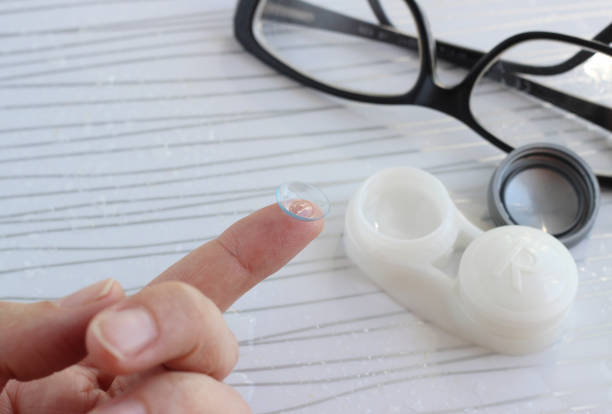Female finger with contact lens, bottle with solution, glasses on white background, selective focus
