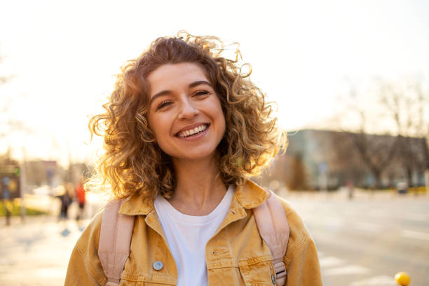 portrait of young woman with curly hair in the city - women smiling blond hair human face imagens e fotografias de stock