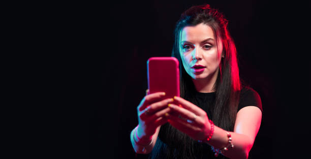 istock Young girl posing with smart phone in her hands, making selfie on black background. Studio shots, copy space for text 1218228981