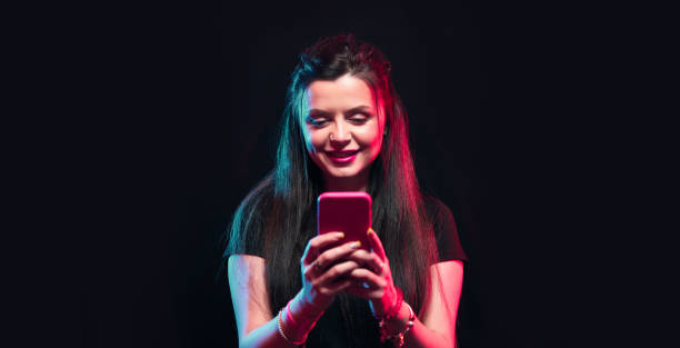 istock Young girl posing with smart phone in her hands, making selfie on black background. Studio shots, copy space for text 1218229048
