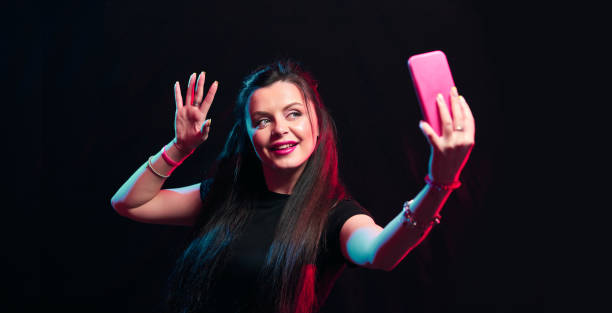 istock Young girl posing with smart phone in her hands, making selfie on black background. Studio shots, copy space for text 1218229131