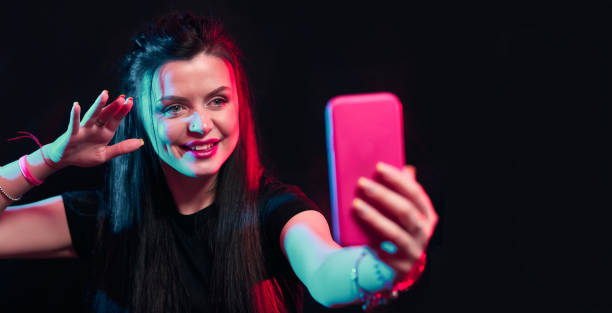 istock Young girl posing with smart phone in her hands, making selfie on black background. Studio shots, copy space for text 1218229158
