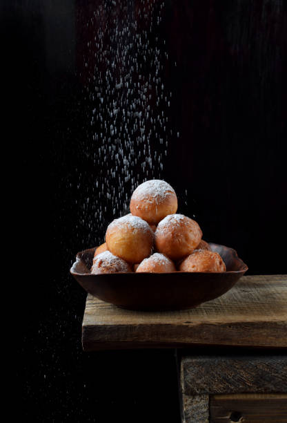 Donut balls in a clay bowl sprinkled with sugar powder on the edge of the wooden table Donut balls in a clay bowl sprinkled with sugar powder on the edge of the wooden table against black background beignet stock pictures, royalty-free photos & images