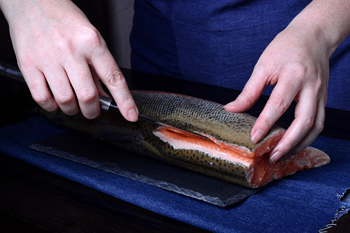 Cook is cutting carcass of a red fish with a knife on black slate board