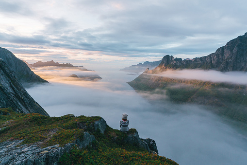 Young Caucasian woman  sitting and looking at  Senja island in fog