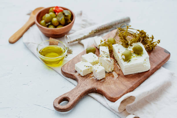 Fresh feta cheese with herbs and olives over curing board stock photo