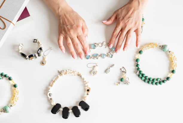 руки женщины средних лет касаясь различных драгоценностей вид сверху - sewing item craft jewelry necklace стоковые фото и изображения
