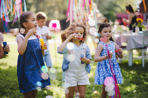 Small children outdoors in garden in summer, playing with bubbles. A celebration concept.