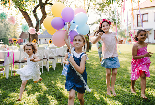 Small children outdoors in garden in summer, playing with balloons. A celebration concept.