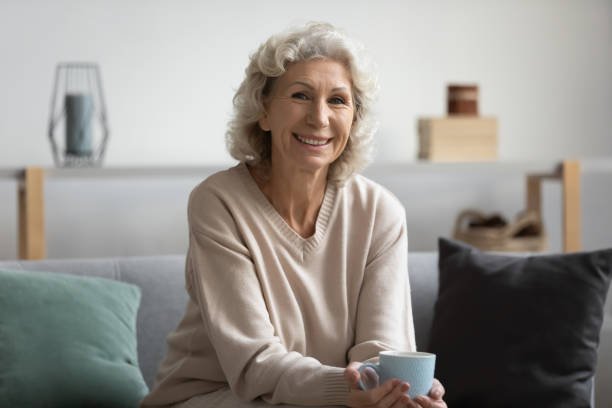 istock Smiling older woman sitting on sofa with cup of tea. 1218234370