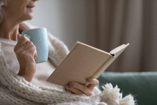 istock Smiling elderly senior woman drinking tea, reading paper book. 1218234420
