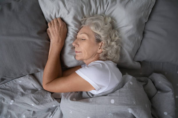 Happy mature woman sleeping on soft pillow under blanket. Above top view calm peaceful elderly mature hoary woman sleeping on soft pillow under blanket, enjoying sweet dreams at night. Happy middle aged granny lying on side, resting in comfortable bed alone. deep stock pictures, royalty-free photos & images