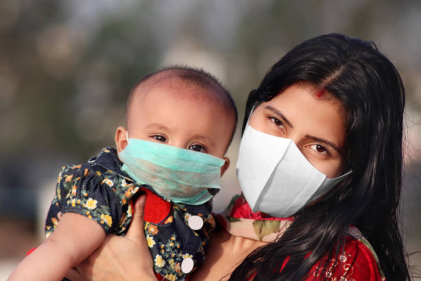 portrait of mother and baby daughter covering face with pollution mask against covid-19 or coronavirus - babies and children close up horizontal looking at camera imagens e fotografias de stock