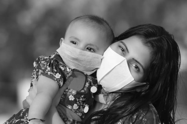 portrait of mother and baby daughter covering face with pollution mask against covid-19 or coronavirus - babies and children close up horizontal looking at camera imagens e fotografias de stock