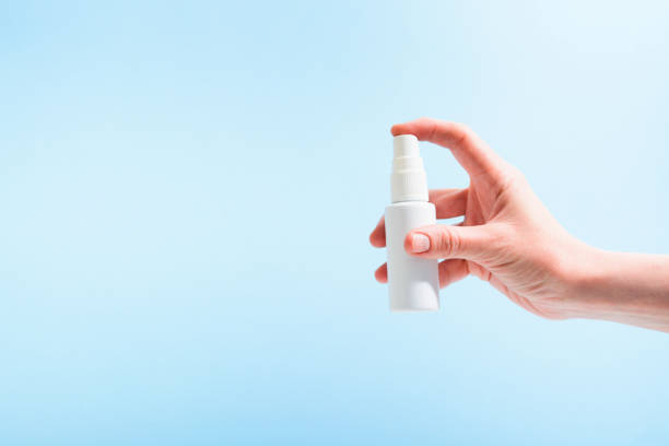 la mano de la mujer sostiene la botella de plástico blanco con el aerosol sobre el fondo azul - perfume bottle scented cosmetics fotografías e imágenes de stock