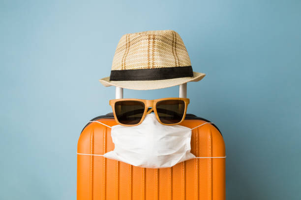 valigia con cappello, occhiali da sole e maschera medica protettiva su sfondo blu pastello minimale coronavirus creativo covid-19 concetto di viaggio. - airplane travel commercial airplane isolated foto e immagini stock