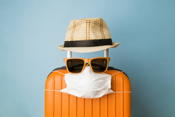 koffer met hoed, zonnebril en beschermend medisch masker op pastelblauwe achtergrond minimaal creatief coronavirus covid-19 reisconcept. - baggage fotos stockfoto's en -beelden