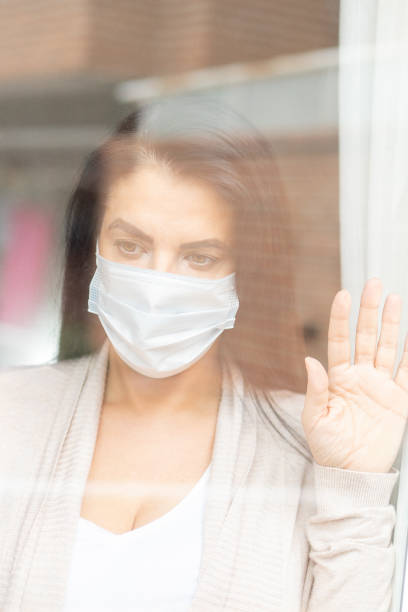 istock woman with sanitary mask through the window 1218252995