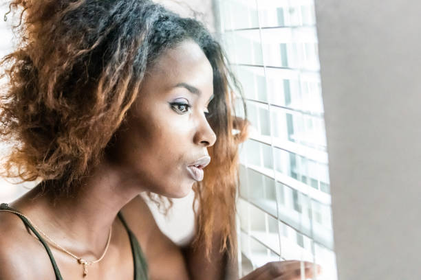 istock Serious African descent woman locked down alone because Covid-19 looking through a window 1218255698