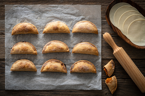 Roasted sweet potato patties pie empanadas food homemade on rustic wood with sugar on it over baking paper and rolling pin