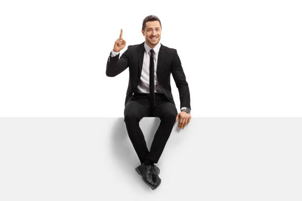 istock Young man in a suit sitting on a panel and pointing upwards 1218255916