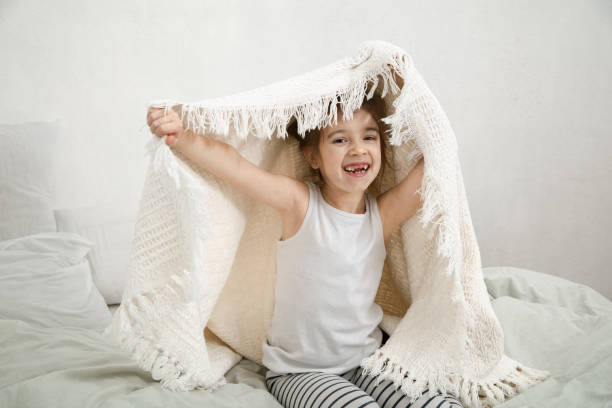 istock Cute little girl playing in bed with a blanket. 1218256294