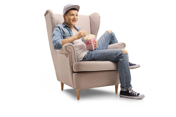 guy seated in an armchair with a box of popcorn - remote television movie box imagens e fotografias de stock