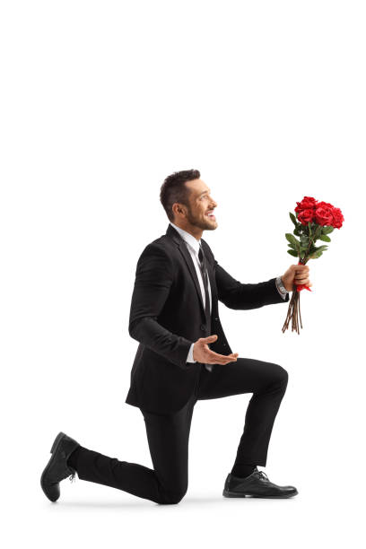 istock Young handsome man kneeling with a bunch of red roses 1218258315