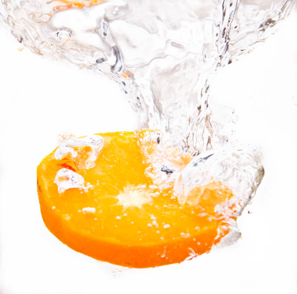 a slice of asn orange falls into a fresh glass of water and makes beautiful bubbles, a kind of freshness
