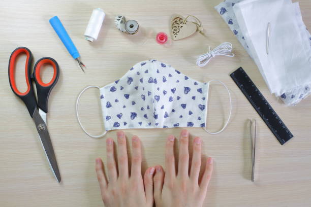 Female hands on the table, a protective mask and sewing tools. Stitched rag mask. stock photo