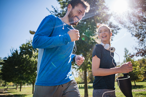Cheerful athletic couple jogging outdoors in a public park, living a healthy lifestyle.