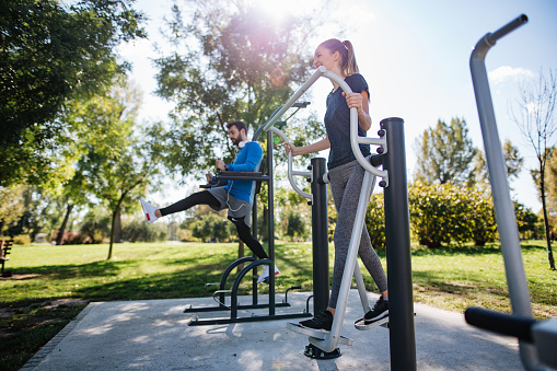 Cheerful athletic couple exercising outdoors in a public park gym, living a healthy lifestyle.