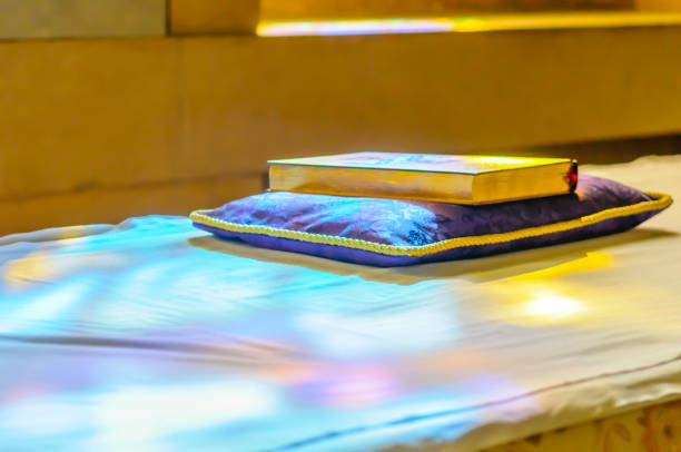 book of common prayer, lit by light from a stained glass window, resting on a purple cushion. - church stained glass hymnal glass imagens e fotografias de stock