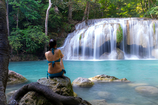 Traveler with blue swimsuit sit relax at Erawan Waterfall and natural in Kanchanaburi province Thailand. Erawan Waterfall Is a beautiful and famous water fall.