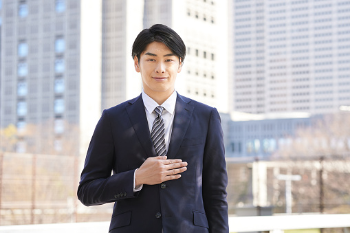 A Japanese male businessman standing in the background of a building.