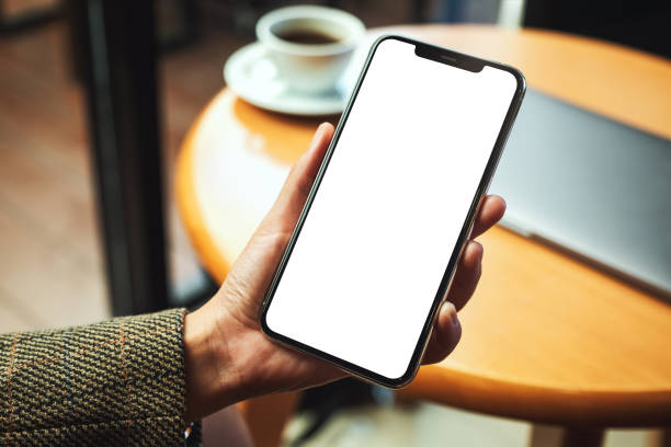 istock a woman's hand holding mobile phone with blank white desktop screen with laptop and coffee cup on table 1218309560