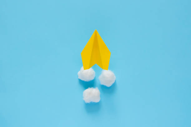 istock Yellow paper airplane moving on the clouds with blue background. 1218317229