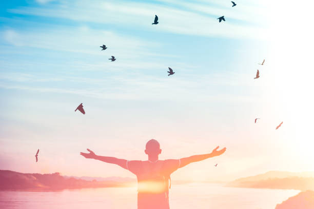 istock Happy backpack man raise hand up and birds flying on sunset sky at river background. 1218318546