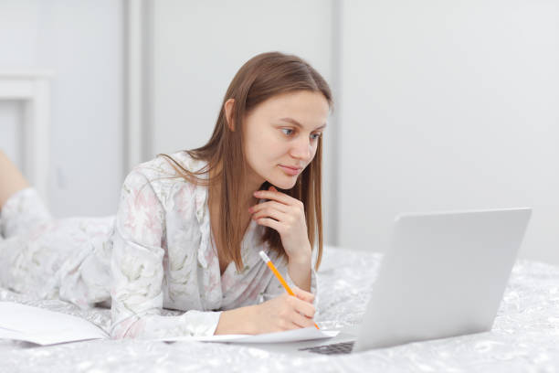 istock Beautiful young woman working, using laptop computer and makes notes in the bedroom at home. Freelancer. Writing, typing. Girl checking social apps. Communication and technology concept 1218337685