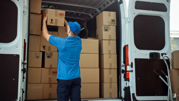 istock Courier Takes out Cardboard Box Package from Delivery Van Full of Parcels, Delivering Postal Parcel. 1218341235