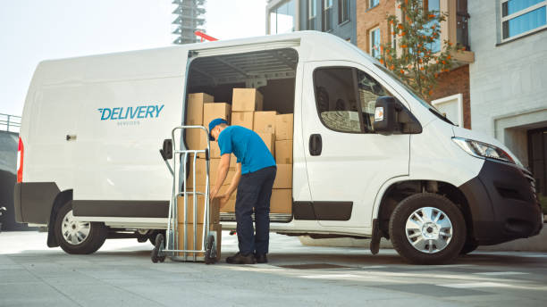 istock Courier Takes out Cardboard Box Package From Opened Delivery Van Side Door. Professional Courier / Loader helping you Move, Delivering Your Purchased Items Efficiently 1218341300