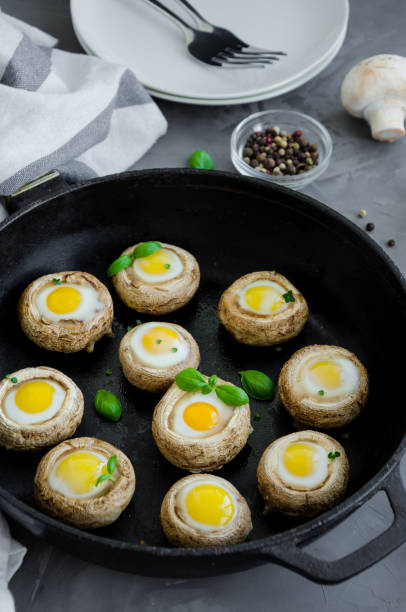 funghi ripieni al forno con uova di quaglia con foglie di timo e basilina in una vecchia padella di ghisa su uno sfondo di cemento scuro. antipasto pasquale. orientamento verticale. - edible mushroom stuffed portabello mushroom vegetarian food foto e immagini stock