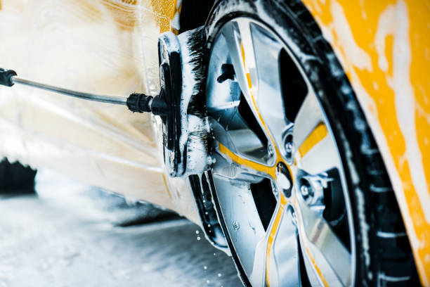 Car washing close up. Cleaning a car with foam brush and high preasure water Man washing a car using brush and soap or foam. Manual cleaning modern aloy wheel in selective focus. splash screen stock pictures, royalty-free photos & images