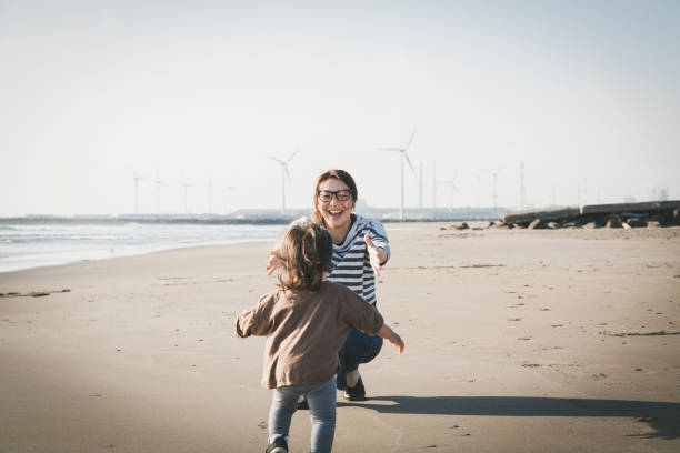 Mother and baby relaxed on the beach close to wind farm Asian family playing in the beach where there is wind power station in the background. ocean life stock pictures, royalty-free photos & images