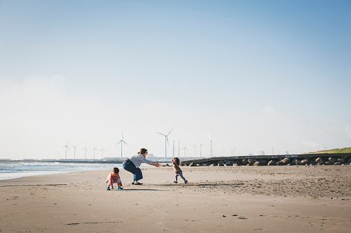 Asian family playing in the beach where there is wind power station in the background.